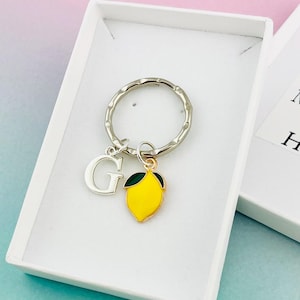 May include: A silver keyring with a lemon charm and a letter G charm. The keyring is in a white box with a message that says "Your Message Here".