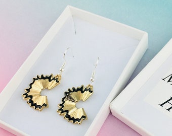 May include: A pair of gold pencil sharpener earrings with black detailing, displayed in a white gift box with the text "Your Gift Message Here".