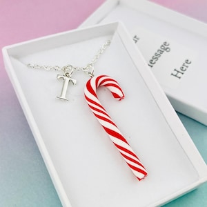 May include: A silver necklace with a candy cane pendant and a letter "T" charm, presented in a white gift box. The candy cane is red and white striped. The box lid is open, revealing the message "message Here".