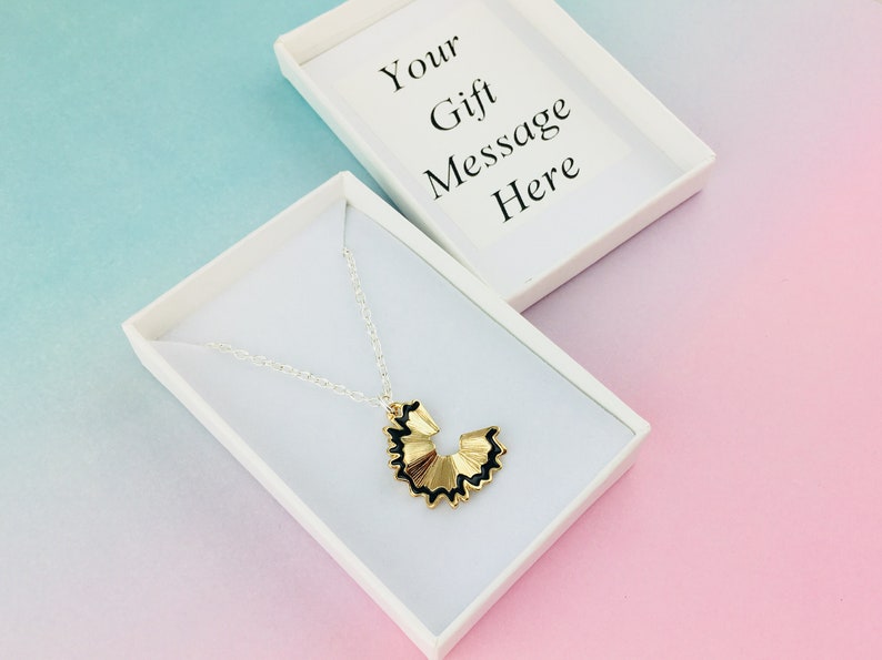 May include: A gold pencil sharpener necklace in a white gift box. The box has the text "Your Gift Message Here" on the lid.