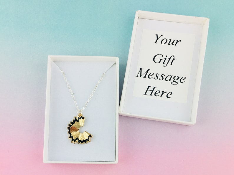 May include: A gold pencil sharpener charm necklace in a white gift box. The box has a white card with the text "Your Gift Message Here".