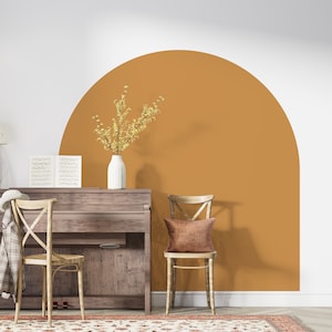 Puede incluir: Un piano de madera con un acabado marrón se encuentra frente a una pared con un gran semicírculo pintado en un amarillo mostaza cálido. Dos sillas de madera con asientos tejidos y un jarrón de flores amarillas también están en la habitación.