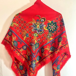 May include: A red square scarf with a paisley pattern in shades of green, blue, yellow, and white. The scarf has a fringed edge.