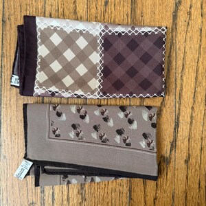 May include: Two folded silk pocket squares. One features a brown and tan checkered pattern with white stitching. The other is taupe with a dark border and a repeating abstract design in black and white.