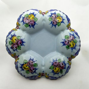 May include: A light blue ceramic dish with six sections, each decorated with a floral design in shades of yellow, pink, and green. The dish has a scalloped edge and a blue and white border.