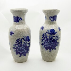 May include: Two white ceramic vases with blue floral designs. The vases have a crackled glaze finish.