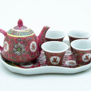 May include: A pink and white porcelain tea set with a teapot, four cups, and a tray. The teapot and cups feature Chinese characters.