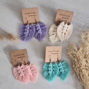 Puede incluir: Cuatro pares de pendientes de borla hechos a mano en morado, beige, rosa y turquesa. Cada par está unido a una tarjeta con el texto "Handmade with love".