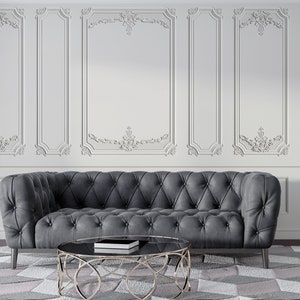 May include: A grey button-backed sofa with a round coffee table and a patterned rug. The coffee table has a black glass top and a gold metal base. The wall behind the sofa is white with decorative moulding.