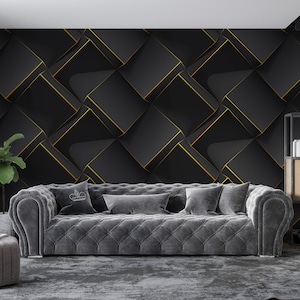 Puede incluir: Un salón moderno con un sofá gris capitoné con cojines decorativos, un otomán a juego y una pared de acento geométrica negra y dorada. Una planta en maceta y una estantería de madera completan la decoración. La habitación tiene una ventana grande con cortinas grises.