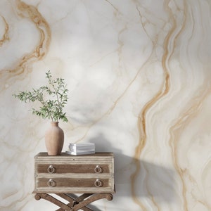 Può includere: Una scena decorativa con un piccolo comò in legno a due cassetti e maniglie ad anello in metallo. Un vaso con piante verdi e una pila di libri sono appoggiati sopra. Lo sfondo è una parete in marmo bianco e oro.