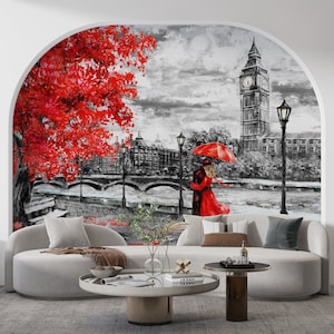 Puede incluir: Un gran mural que representa una escena romántica en Londres. La obra de arte muestra el Big Ben, una pareja bajo un paraguas rojo y un árbol rojo vibrante sobre un fondo en blanco y negro. El mural está instalado sobre un sofá blanco curvo.