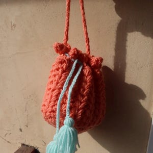 Puede incluir: Bolso de ganchillo hecho a mano, color coral, con cierre de cordón y borlas azul claro. El bolso tiene un patrón de puntada texturizada y un asa coral a juego. Este bolso pequeño y elegante es perfecto para llevar objetos pequeños.