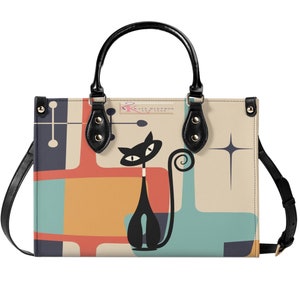 May include: A black leather tote bag with a retro-style design featuring a black cat with a curled tail, geometric shapes in shades of blue, orange, and red, and a white background. The bag has a black top handle and a detachable shoulder strap.