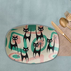Puede incluir: Un plato ovalado blanco para servir con un diseño retro que presenta gatos negros y formas abstractas verdes y rosas.
