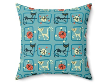 May include: A turquoise blue throw pillow with a repeating pattern of black and white cats, red and white atomic symbols, and blue squares.