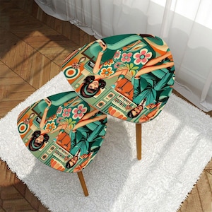 May include: Two retro-style side tables with a mid-century modern design. The oval tabletops feature a colorful illustration of a woman in a floral dress and a man in a suit. The tables have wooden legs and are placed on a white rug.