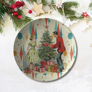 Könnte beinhalten: Ein Weihnachtsteller im Vintage-Stil mit einem Paar, das neben einem geschmückten Weihnachtsbaum steht. Der Teller hat einen weißen Hintergrund mit einem Muster aus roten, blauen und grünen Diamanten. Das Paar ist festlich gekleidet und hält Geschenke. Der Teller ist perfekt, um Ihrem Weihnachtsdekor einen Hauch von Retro-Charme zu verleihen.