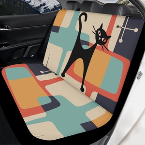 May include: A black cat with a retro mid-century modern design on a car seat cover. The design features geometric shapes in shades of orange, yellow, blue, and beige.