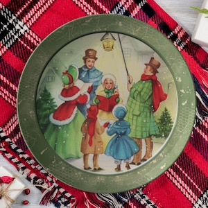 May include: A green round plate with a vintage Christmas scene of carolers singing in the snow. The plate has a gold rim and a textured surface.