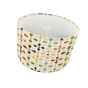 Pode incluir: Abajur cil&iacute;ndrico com fundo creme e um padr&atilde;o floral repetido em v&aacute;rias cores, incluindo verde, azul, laranja e castanho. O interior &eacute; branco e a estrutura met&aacute;lica &eacute; vis&iacute;vel.