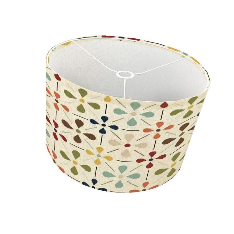 Pode incluir: Abajur cil&iacute;ndrico com fundo creme e um padr&atilde;o floral repetido em v&aacute;rias cores, incluindo verde, azul, laranja e castanho. O interior &eacute; branco e a estrutura met&aacute;lica &eacute; vis&iacute;vel.
