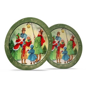 May include: Two round green coasters with a gold rim and a vintage Christmas scene of people singing carols in the snow. The scene includes a street lamp, a house, and a Christmas tree.