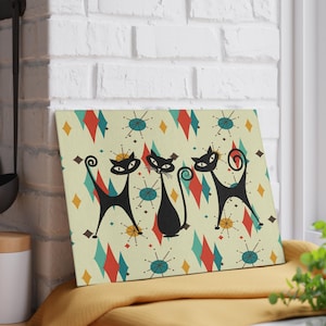 May include: A retro-style print featuring three black cats with stylised tails against a background of yellow, red, blue and green geometric shapes.