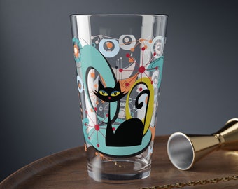 May include: A tall glass with a black cat design. The cat is surrounded by a blue, green, and orange abstract pattern. The glass is clear and has a rounded bottom.