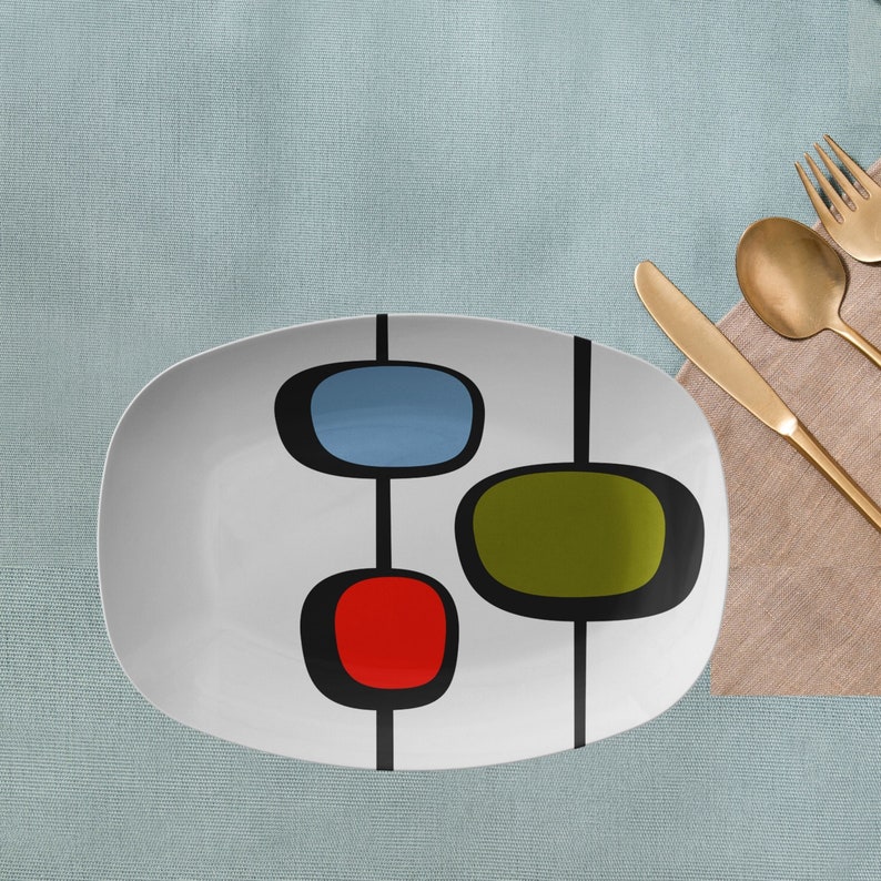 May include: White oval serving platter with a mid-century modern design featuring abstract shapes in red, blue, green, and black.