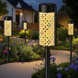 Puede incluir: Luces de camino para jardín con postes negros y pantallas estampadas. Las pantallas tienen un fondo crema con un diseño floral repetido en rojo, verde, marrón y amarillo. Las luces están instaladas a lo largo de un camino curvo en un jardín.