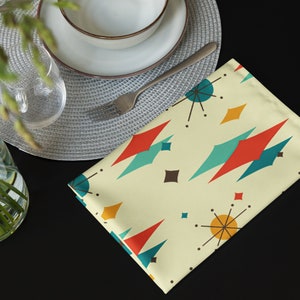 May include: A yellow placemat with a geometric pattern of red, blue, and brown shapes. The placemat has a retro mid-century modern design.