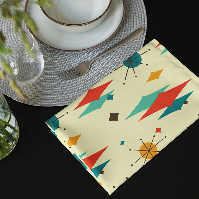 May include: A yellow placemat with a geometric pattern of red, blue, and brown shapes. The placemat has a retro mid-century modern design.