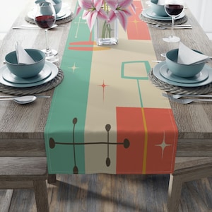 May include: A teal, orange, and brown geometric patterned table runner with a mid-century modern design. The runner is on a wooden table with two place settings on each side.