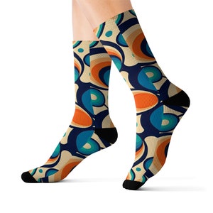 May include: A pair of socks with a retro-inspired pattern featuring orange, blue, and teal circles on a cream background.