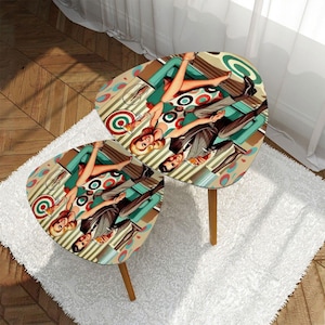 May include: Two retro-style side tables with a mid-century modern design. Each table features a triangular top with a colourful illustration of a couple in vintage attire. The tables have wooden legs and are set on a white rug.