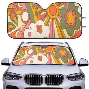 Könnte beinhalten: Ein Autosonnenschutz mit einem Retro-Blumenmuster. Der Sonnenschutz hat ein Muster aus Blumen, Sonnenstrahlen und abstrakten Formen in Orange-, Gelb-, Rosa- und Grüntönen. Der Sonnenschutz wird sowohl separat als auch in einem Auto gezeigt.