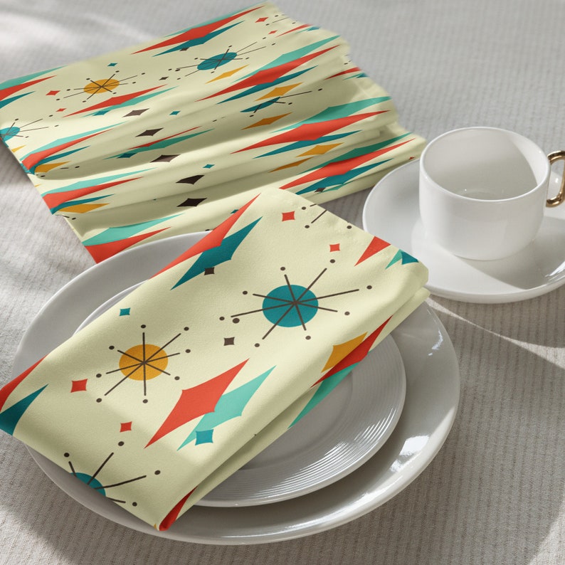 May include: A set of four yellow napkins with a mid-century modern geometric pattern featuring red, blue, and orange accents. The napkins are folded and placed on a white plate.