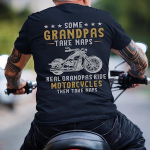 May include: A black t-shirt with a white graphic of a motorcycle and the text "Some Grandpas Take Naps. Real Grandpas Ride Motorcycles Then Take Naps."