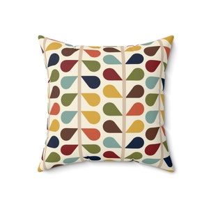 May include: A square throw pillow with a cream-colored background and a repeating pattern of teardrop shapes in shades of red, orange, yellow, green, blue, and brown. The teardrop shapes are arranged in rows, with each row offset from the one above it.