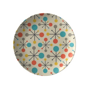 May include: A white ceramic plate with a mid-century modern design featuring a repeating pattern of grey, yellow, blue, and orange circles and starbursts.