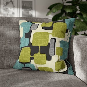 May include: A decorative throw pillow with a geometric pattern in shades of green, blue, gray, and black. The pillow has a white background and a textured fabric.