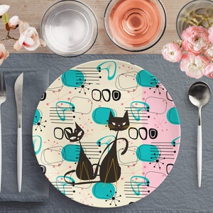 Könnte beinhalten: Ein weißer Keramik-Dinnerteller mit einem Mid-Century-Modern-Design mit schwarzen Katzen, rosa und blauen abstrakten Formen und weißen Sternen auf cremefarbenem Hintergrund.