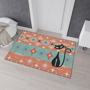 May include: A rectangular area rug featuring a repeating pattern of starbursts and diamonds in shades of coral, teal, and white. A stylized black cat with large yellow eyes and a curled tail is positioned on the right side of the rug.
