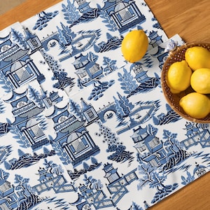 Pode incluir: Caminho de mesa de tecido azul e branco com um design chinês tradicional. O caminho de mesa apresenta um padrão repetitivo de pagodes, pontes e flores.