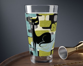 May include: A tall glass with a black cat design on a green, blue, and white geometric background. The glass is made of clear glass and has a wide mouth.