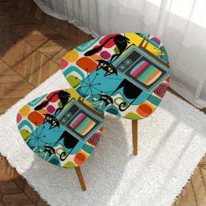May include: Two retro-style nesting tables with a colorful abstract design featuring cats and a television set. The tables have a blue, green, yellow, orange, and red color scheme. The table legs are made of wood.
