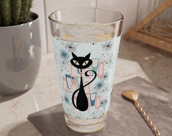 Puede incluir: Un vaso de vidrio transparente con un diseño de gato negro. El gato está de pie sobre un fondo azul con formas geométricas rosas y verdes y estrellas blancas. El vaso está lleno de hielo y una bebida.