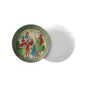May include: A green ceramic plate with a vintage Christmas scene of carolers singing in the snow. The plate has a gold rim and a white background.
