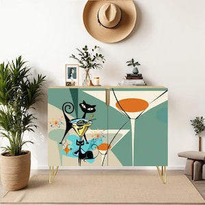 May include: A mid-century modern cabinet with a teal and cream color scheme. The cabinet doors feature a retro illustration of black cats with martini glasses and atomic age-inspired designs. The cabinet has gold-colored legs and is set against a neutral background.